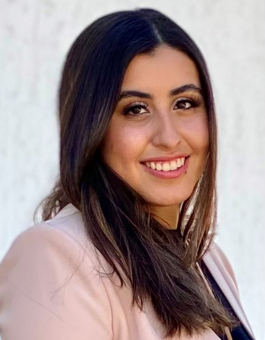 Smiling headshot of Carolina Gonzalez with long dark hair wearing blush blazer, neutral background