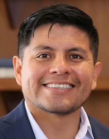 Luis M Peña-Lévano headshot photograph of a smiling man in a suit with warm blurred background